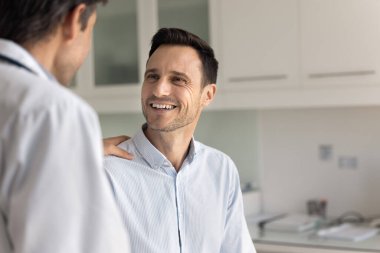 Pozitif doktor erkek hastaya olumlu haberler veriyor, sağlık raporunu, sağlık muayenesi sonuçlarını, omzuna destek, cesaret ve güven verici hareketlerle dokunuyor.