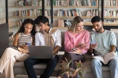 Akran öğrenmede modern teknoloji. Çok ırklı lise öğrencileri kütüphanede verimli bir işbirliği içinde çalışarak bilgi paylaşımı yapıyor. Cihazları kullanarak fikir alışverişinde bulunuyor.