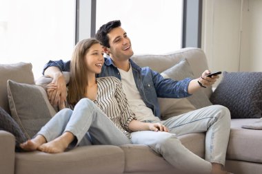 Çift koltukta rahat bir şekilde oturuyor, rahat bir şekilde dinleniyor, TV seyrediyor, uzaktan kumandayı elinde tutuyor, romantik filmi seçiyor, sevgili kadınla keyifli vakit geçiriyor ve hafta sonu eğlencesine katılıyor.