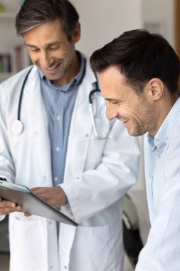 Beyaz üniformalı Latin erkek doktorun dikey yakın görüntüsü pano tutuyor ve hastalara sağlık test sonuçlarını, tıbbi kayıtları ya da tedavi planını gösteriyor. İyileşme, sağlık danışmanlığı