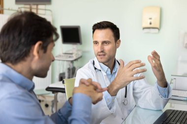 İspanyol erkek doktor klinik muayenehanesine yaptığı ziyarette hastaya profesyonel sağlık tavsiyesi sunar, reçeteli ilaçların dozajını açıklar, teşhis veya sağlık testi sonuçları hakkında konuşur