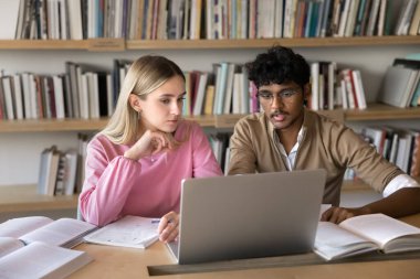 Akran işbirliği. Kütüphane masasında çalışan iki farklı etnik çeşitlilikteki Z sınıfı öğrenci arkadaşları, ortak bilimsel proje oluşturmak için not defteri kâğıdı kaynaklarını kullanarak sorunlu çözümü tartışmak için sınavlara birlikte hazırlanıyorlar.