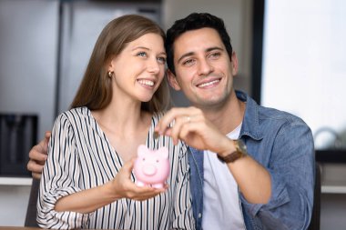 Genç ve güzel eşler, gelecekteki harcamaların, ekonomik istikrarın, finansal okur yazarlığın ve akıllı para yönetiminin sembolü olarak evlerinde oturmuş pembe kumbaralara bozuk para koyuyorlar. Aile bütçesi