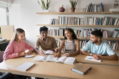 Neşeli akran öğrenimi. 4 etnik çeşitliliğe sahip genç öğrenci kütüphane masasında oturup edebiyat tartışırken akademik proje hakkında şaka yaparken eğleniyorlar. Canlı sohbet sırasında kahkahalar atıyorlar.