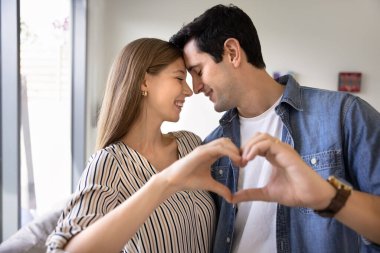 Birbirlerine aşık güzel bir çift içeride durup kucaklaşıyorlar, alınlarına dokunuyorlar, şefkatin tadını çıkarıyorlar gözleri kapalı, parmaklarını kalp simgesinde birleştiriyorlar. Seviyorum imzanı, Sevgililer Günü kutlaması