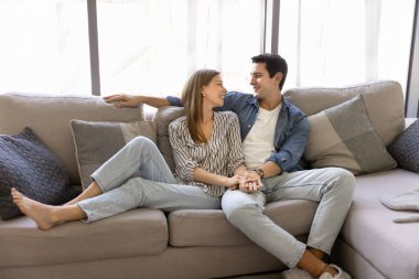 Rahat çift kanepede rahatça oturur, güler yüzlü ve kurşunlu konuşmalar modern oturma odasında birlikte zaman geçirirler. Genç ev sahibi aile rahat bir kanepede dinleniyor, hafta sonları evde sohbetin tadını çıkarıyor.