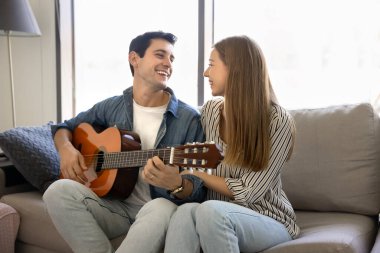 Genç Latin çift rahat bir kanepede birlikte oturup müzik dinlemekten zevk alıyor. Bir erkeğin gitar çaldığı, sevgilisine evde romantik bir şarkı söylediği samimi bir an. Romantizm, ilişkiler