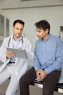 Ciddi pratisyen hekim ya da kardiyolog, elektronik reçete, tıbbi tarama ya da muayene sonuçlarını açıklarken, modern dijital tablet aygıtı kullanan erkek hastalara profesyonel danışma hizmeti sunmaktadır.