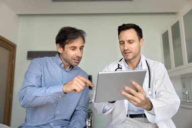 Beyaz önlüklü, orta yaşlı İspanyol doktor elinde dijital tablet, bilgiyi açıklıyor, sağlık testi sonuçlarını veya tedavi seçeneklerini hastalara inceliyor. Teknoloji destekli sağlık hizmetleri danışmanlığı