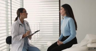 Beyaz önlük giyen, pano tutan, not alan, tıbbi form dolduran, hasta muayenesi sırasında hastayı dinleyen ve hastanın semptomlarını ya da sağlık sorunlarını açıklayan kadın doktor.