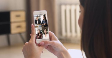 Çeşitli iş adamlarının görüntülendiği akıllı telefon ekranı video konferansına katılıyor, kadınların omuzları üzerinden görüş alıyor modern cihazlar. Video konferans uygulaması ve dijital iletişim kullanan sanal toplantı olayı