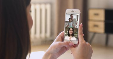 Çeşitli insanlar video konferansına katılıyor, akıllı telefon ekranı kadın omzunun üstünden görünüyor, kapatın. Aile arasında dünya çapında iletişim, kişisel haberleri paylaşın uygulamayı kullanarak arkadaşlarınızla sanal buluşmanın keyfini çıkarın