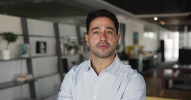 Açık ofis alanında poz veren başarılı genç İspanyol işadamı, kameraya bakıyor, mutlu oluyor, gülümsüyor, tek başına çalışıyor. Latin profesyonel adam, iş adamı lideri portresi