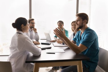 Doktor çözüm öneriyor. Bin yıllık erkek cerrah takım brifinginde masada oturan çok kültürlü meslektaşlarıyla konuşuyor. Yaratıcı fikri açıkla. Hasta sağlık planında yenilikçi değişiklikler öneriyor.