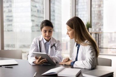 Tıpta etkileşimli öğrenme. Klinikteki genç kız stajyer öğrencilere dijital tablet ekranındaki tıbbi sorunu açıklayan öğretim görevlisi.
