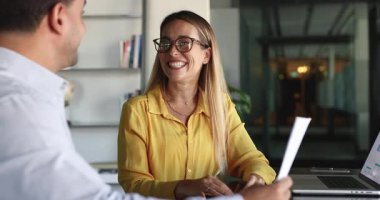 Olumlu genç kadın finans uzmanı, erkek meslektaşına evrak içeriğini açıklıyor, kağıda işaret ediyor, konuşuyor, gülümsüyor, tavsiyelerde bulunuyor, iş yerindeki iş arkadaşına danışıyor.