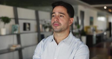 Ciddi, genç, düşünceli Latin iş adamı iş yerinde tek başına çalışıyor, başka yere bakıyor, başarılı iş projesini düşünüyor, kariyer başarısını düşünüyor, mutlu oluyor, gülümsüyor.