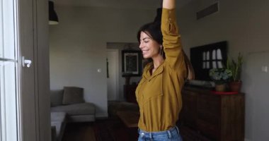 Güzel bir kadın, günlük kıyafetleriyle salonda dans ediyor, popüler şarkılar dinliyor ya da en sevdiği müziği dinliyor, ellerini kaldırıyor, tasasız ve mutlu hissediyor, taşınmayı kutluyor, hafta sonları evde hayatın tadını çıkarıyor.