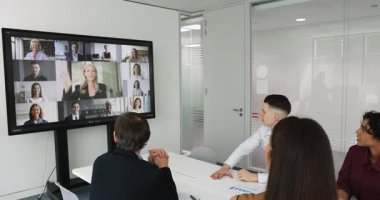 Konferans masasının etrafında toplanan insanlar, uzak takım üyelerinin video çağrısına katıldıklarını, olgun profesyonel kadınların konuşmalarını dinlediklerini, şirket hedeflerini veya stratejilerini paylaştıklarını gösteriyorlar.