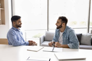 İş yerinde iş birliği. Değişik yaşlarda gülümseyen çok ırklı erkek arkadaşlar fikir alışverişinde bulunurlar beyin fırtınası içgörüleri iş ilişkilerini tartışırlar evrak işlerinde işbirliği yaparlar rahat yaratıcı ofiste masada otururlar.