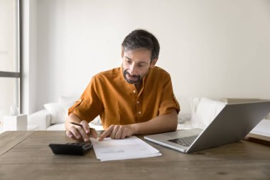 Hesaplamalar yapıyorum. Çok düşünceli, orta yaşlı serbest çalışan bir erkek. Küçük işletme sahibi, iş yerinde oturuyor. Ev kredisi faiz hesaplarını hesaplıyor.