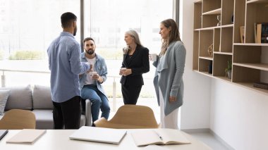 Kahve molası sohbetleri. Çeşitli etnik çeşitlilikteki iş adamları sıcak içecek bardaklarıyla toplantı odasında durup iş molası sırasında gayri resmi iletişim tartışmalarının keyfini çıkarıyorlar.