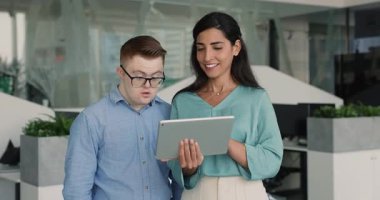 Şirketin çeşitli meslektaşları birlikte tablet kullanıyorlar, ofiste duruyorlar, çevrimiçi ürünleri tartışıyorlar. Latin profesyonel kadın ve Down sendromlu iş adamı takım çalışması için aygıt kullanıyor
