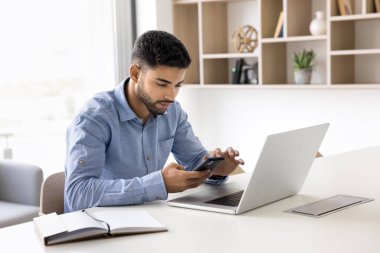 Dijital teknolojiyle ofis işi. Meşgul meşgul milenyum adamı modern şirket çalışanı serbest çalışan girişimci akıllı telefon değiş tokuş bilgileri ile iş yerindeki defter bilgisayarı ile mesajları kontrol et