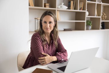 İş yerinde kendine güvenen bir profesyonel. Portre başarılı gülümsüyor orta yaşlı kadın öğretmen satış yöneticisi proje yöneticisi masada oturuyor kağıt çalışma kitabıyla kameraya bakıyor.