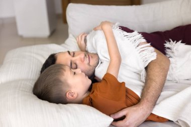 Sıcak aile bağı. Serin portre, tasasız genç baba küçük çocuk, rahat bir kanepede uzanmış sıcak yumuşak ekoseyle kaplanmış, sarılmış, dinlendirici, her gün uyuklayan.