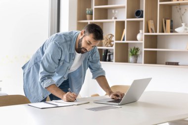 Merkez ofis iş akışı. Çalışma sürecini planlayan görevleri yönetmek için kağıt telif defterine notlar yazarak bilgi için işyeri masa başında çalışan odaklı milenyum adamı