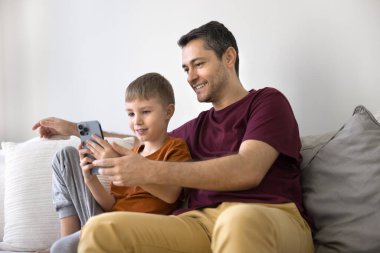 Dijital çağda aile zamanı. Mutlu Milenyum Baba Tween Oğul rahat koltukta rahat rahat modern akıllı telefon ile etkileşime geçin birlikte yeni online oyun oynayın video parşömen blogları eğitim web uygulamasının keyfini çıkarın