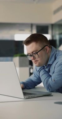 Bilgisayarda çalışan, dizüstü bilgisayarda yazan, ekrana bakan, çevrimiçi ürünü düşünen, içeriği izleyen veya okuyan ciddi erişilebilir şirket Down sendromu çalışanı. Dikey çekim