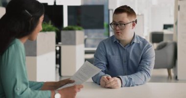 Röportajda Down Sendromlu Aday Adam 'la konuşan, elinde kağıt tutarak gülümseyen olumlu Latin uzman kadın. Çeşitli iş arkadaşları anlaşma metnini tartışıyor