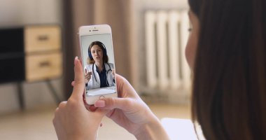 Akıllı telefonu olan bir kadın, tıbbi uzmanla görüntülü görüşme yapmış. Beyaz önlüklü doktorun hastaya teletıp danışmanlığı yaptığı ekranı kapatın. TeleHealth uygulaması
