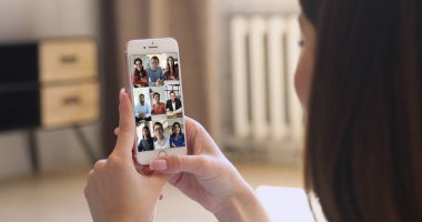 Akıllı telefon, internet bağlantısı ve video konferans uygulaması kullanarak uzak iş ya da kişisel iletişim. Çok ırklı insanlar grup video etkinliğine katılıyor, kadınların omuzlarının üzerinden bakıyorlar.