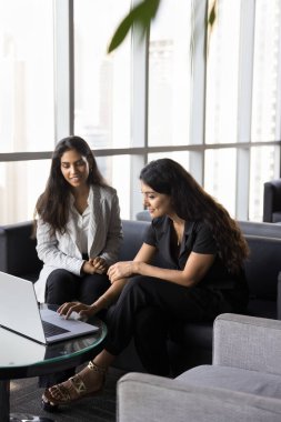 İki çok uluslu kadın modern ofis salonlarında bir araya geldi, dizüstü bilgisayar kullanarak, proje detaylarını inceleyerek, görev atayarak, fikir üreterek veya raporları analiz ederek tartışmalara giriştiler. Profesyonel etkileşim