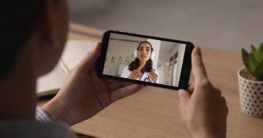 Akıllı telefondan video çağrısına katılan beyaz önlüklü 35 'lik gülümseyen kadın doktor teletıp danışmanlığı, sanal sağlık kontrolü yapıyor. Teletıp uygulaması ve uzaktan sağlık hizmeti