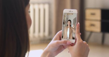 Genç Asyalı kadının yeni evinin anahtarlarını gösterdiği akıllı telefonu tutan kadın, taşınmayı kutluyor, video blogunda kanal içeriği için harika haberler paylaşıyor. Sosyal medya platformu kullanıcısı