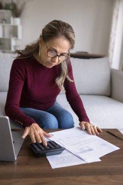 Finansal evraklar ve muhasebe kayıtları. Dikey çekim, gözlüklü yaşlı kadın hesap makinesine bağlı, aile bütçesi, fatura hesapları, aylık kredi ödemeleri,