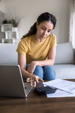 Bağımsız para yönetimi. Finansal evrak işleriyle uğraşan ciddi bir genç kız ofis koltuğunda oturur hesap makineli dizüstü bilgisayar kullanarak kira ödemelerini online çek makbuzları ile yapar.