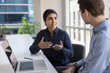 Kendine güvenen Hintli iş kadını toplantı yapıyor, şirket müşterisiyle görüşmeler yapıyor toplantı odasında açık dizüstü bilgisayarla masada oturuyor. İki takım arkadaşı işle ilgili sorunları çözüyor, fikirleri ve çözümleri paylaşıyor