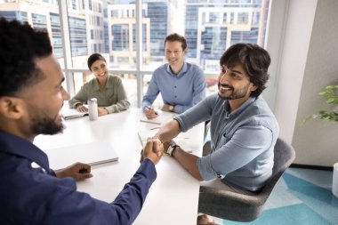 İki çok ırklı iş ortağı konferans odasında çeşitli iş adamlarıyla el sıkışıyor, birbirlerini selamlıyor, görüşmelere başlıyor, işbirliği planlıyor ve ortaklık kuruyorlar.