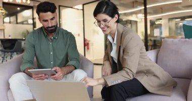 Çeşitli genç iş arkadaşları online ürünü tartışıyor, birlikte dizüstü bilgisayardan video izliyorlar, takım çalışması için bilgisayarda buluşuyorlar, birlikte çalıştıkları koltuklarda oturuyorlar.