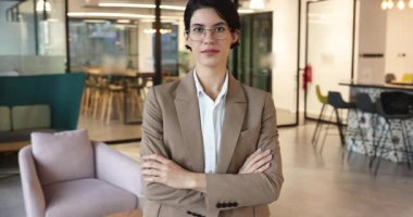 Ofiste elleri bağlı duran, mutlu, pozitif, dişlek gülümsemeli kameraya bakan kendine güvenen genç bir yönetici kadın. Kadın iş adamı, CEO, profesyonel vesikalık.