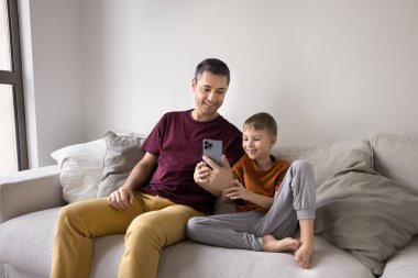 Babam dijital beceriler öğretiyor. Sevgi dolu genç bir baba, küçük oğluyla kanepede oturup çocuk ile birlikte akıllı telefonla eğleniyor. Uygulamalarda çocuklara yardımcı oluyor. Çocuk sörf sitelerini ebeveyn kontrolü altında seyrediyor.