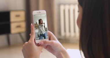 Modern akıllı telefonu elinde tutan genç bir kadın blogcunun dans ettiği internet içeriğini izleyen bir kadın. Sosyal medya platformu ve video paylaşım uygulaması, eğlence, dijital eğlence kullanıcısı