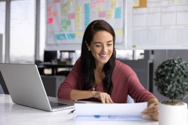 Büyümenin ve verimliliğin tadını çıkarıyorum. Gülümseyen başarılı genç iş kadını veri analisti pazarlamacı çalışma masasında bilgi grafikleriyle ürün satışlarının iyi sonuçlarından tatmin olan makaleler okuyor.