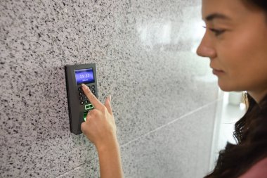 Ev ya da ofis güvenliği. Duvardaki akıllı elektronik alarm sistemindeki tuşlara basan genç bir kadın binaya ya da odaya girmek için kişisel giriş kodu girin. Modern ev teknolojisi kavramı