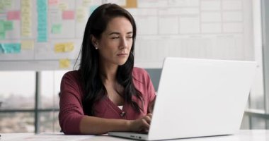 Düşünceli Latin iş projesi lideri kadın ofiste bilgisayar başında çalışıyor, dizüstü bilgisayarda yazıyor, yüzünü çeviriyor, çeneye dokunuyor, masadaki yasal finansal kağıt dökümanına danışıyor.